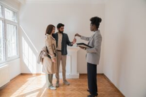 Man and Woman standing in an empty room handed keys from a realtor.