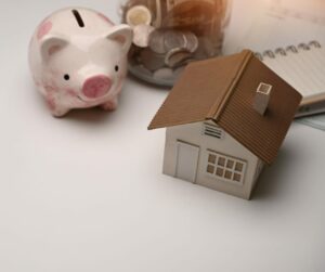 A piggy bank with a model of a simple home and a money jar.