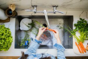 An image of a woman washing vegetables at a sink, highlighting the importance of sewer scope inspections for maintaining a healthy plumbing system.