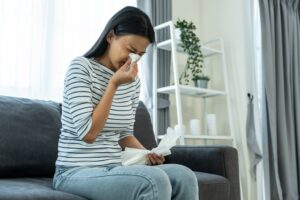 Asian woman having running nose and sneezing in living room sitting on sofa feeling bad and suffer from allergy then put tissue cover her nose while sneeze in house. Need to get a Mold Sampling test of her house.